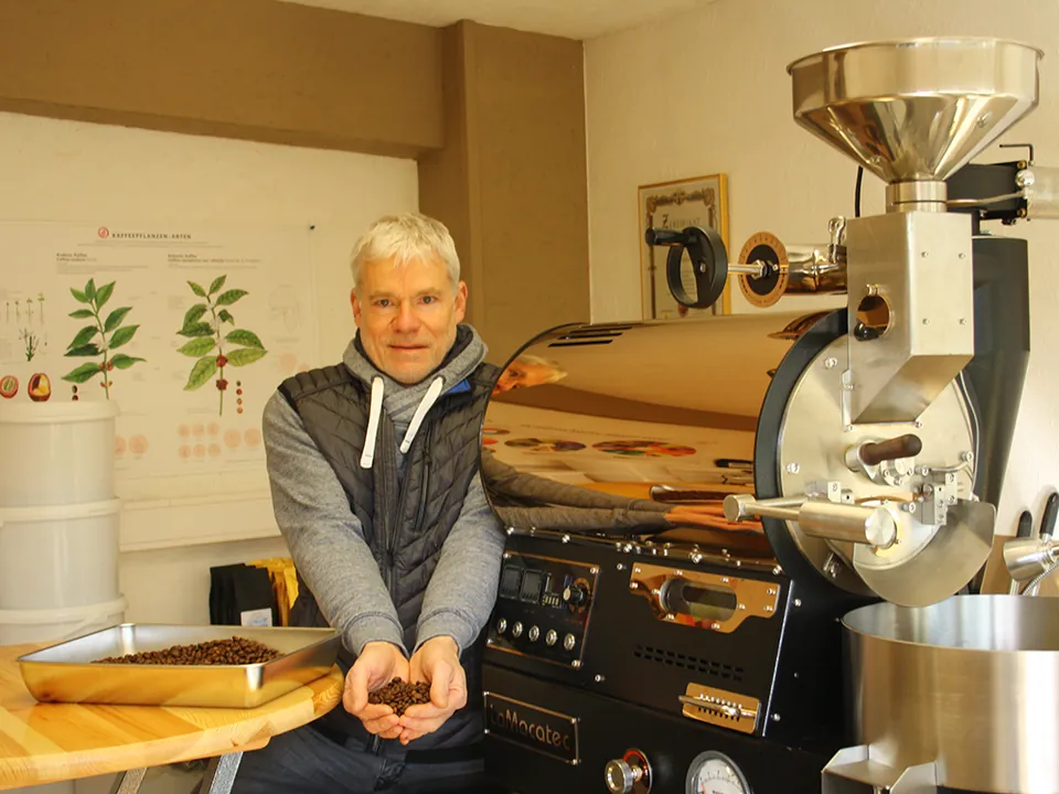 Karsten Klemkow vor seinem Kaffeeröster mit einer Handvoll frisch gerösteter Bohnen